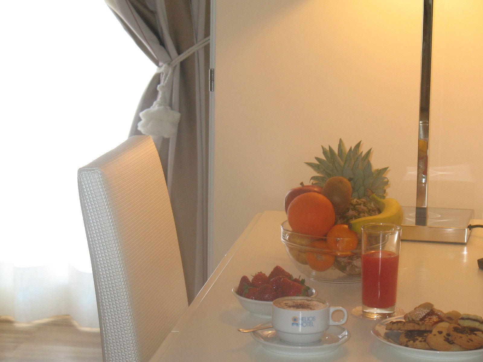 Una mesa de comedor con un frutero, un vaso de jugo, un plato de galletas y una taza de café.