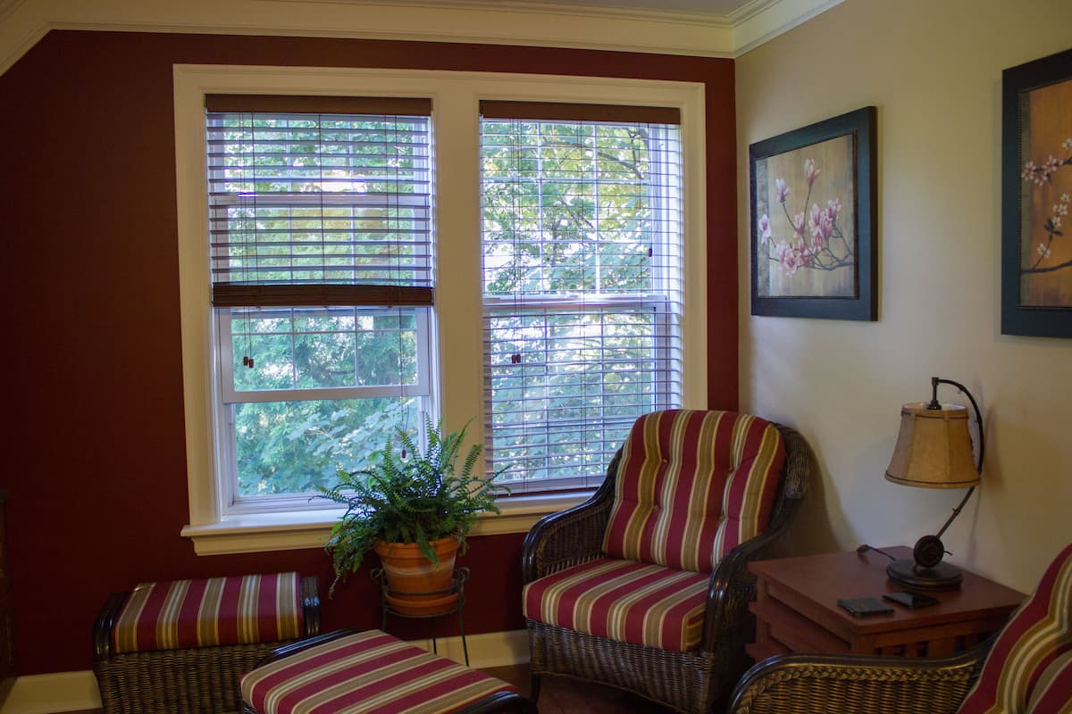 A room with a large window, wicker furniture, a potted plant, and a lamp.