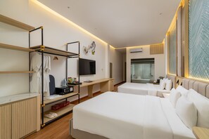 A hotel room with two beds, a TV, a desk with a computer, a wardrobe, and a shower area.