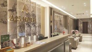 A hotel reception area with a marble wall, a reception desk, and a seating area with a vase of flowers.