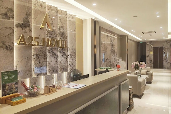 A hotel reception area with a marble wall, a reception desk, and a seating area with a vase of flowers.