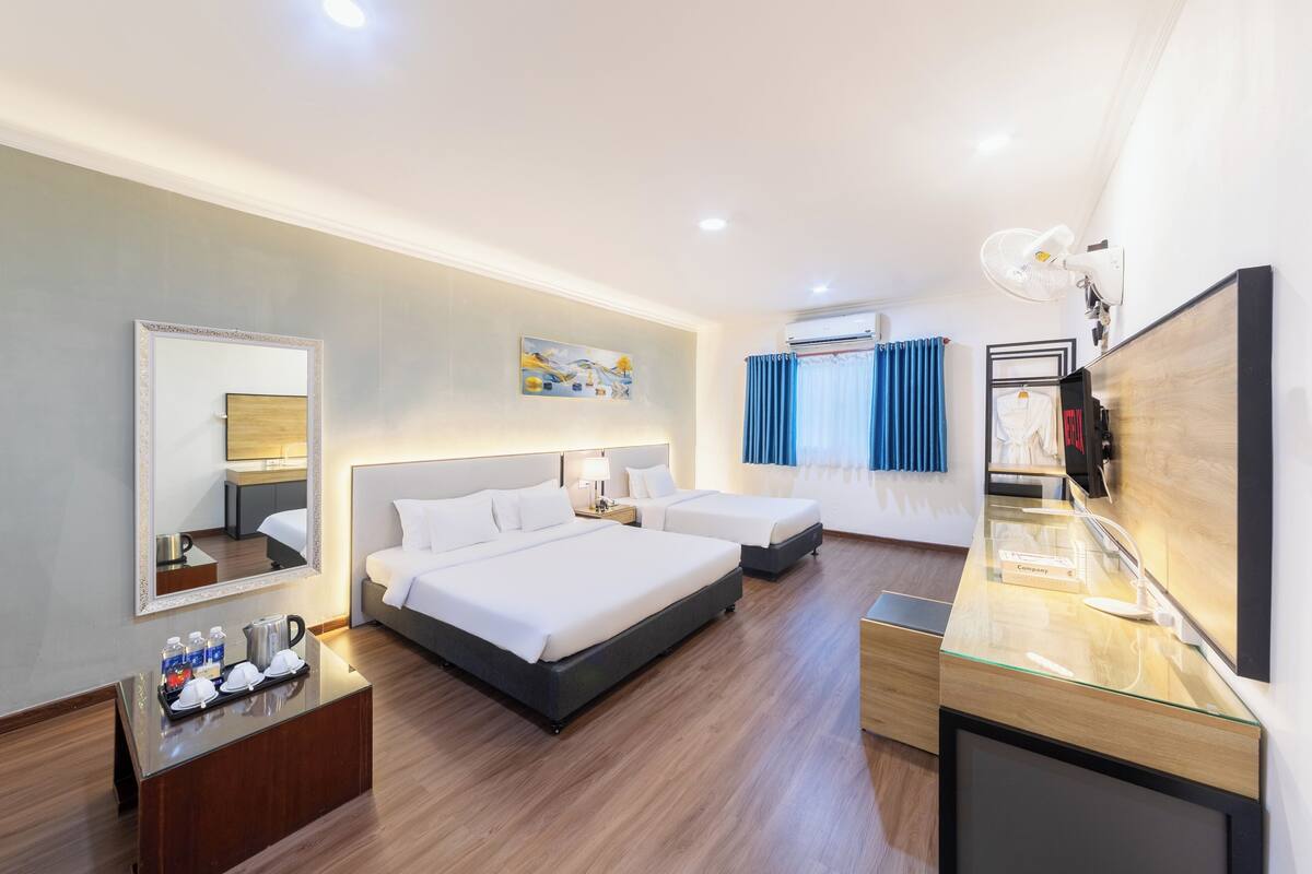 A hotel room with two beds, a desk with a glass top, a mirror, and a painting on the wall.
