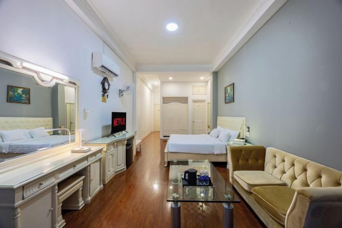 A hotel room with two beds, a sofa, a glass coffee table, and a TV.