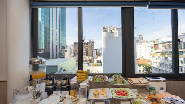 A breakfast buffet with various food items and a juice dispenser, set against a city view.