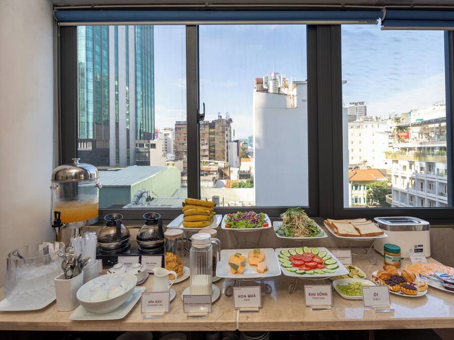 Um buffet de café da manhã com diversas opções de comida e um dispensador de sucos, com vista para a cidade.