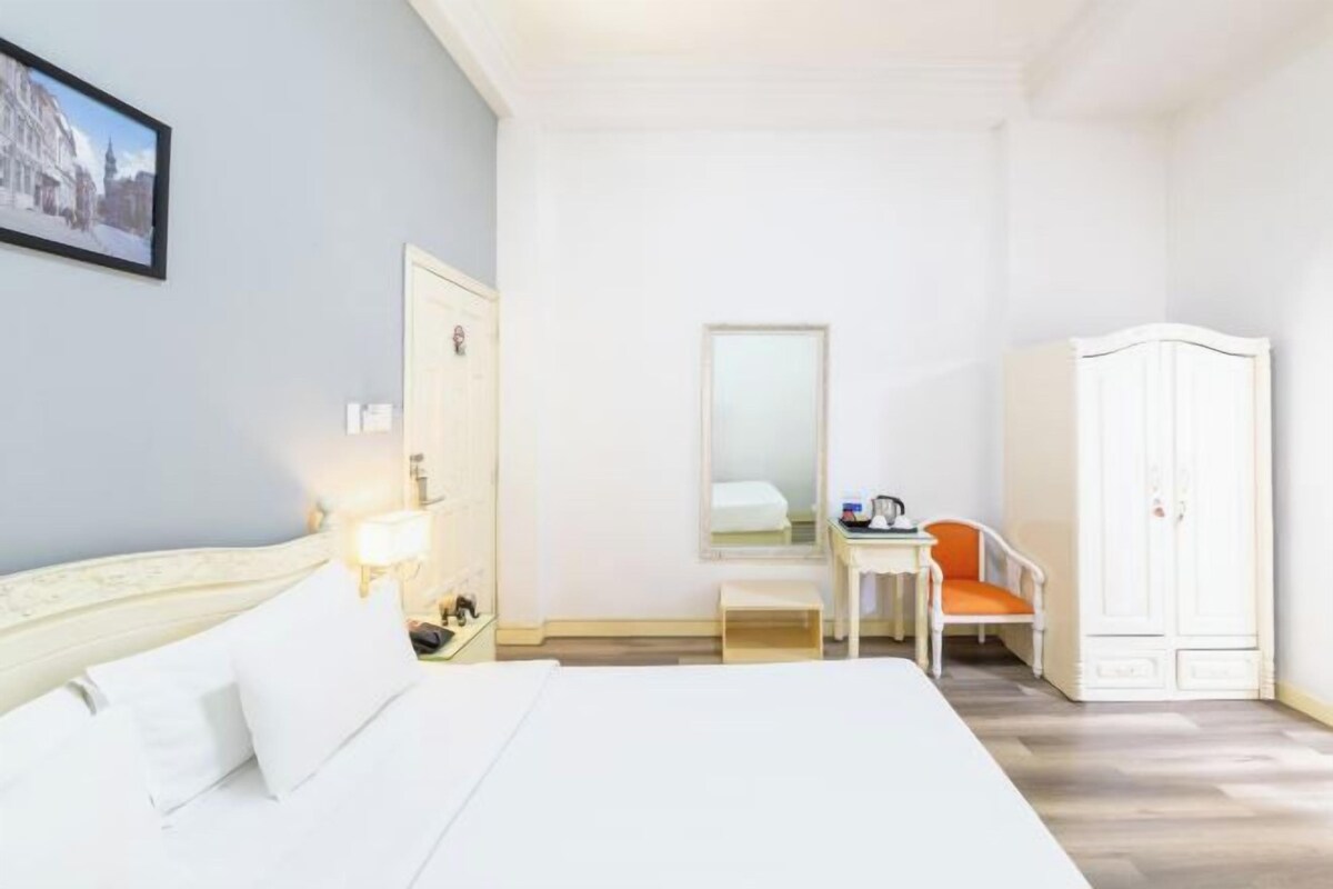 Ett hotellrum med en säng, ett skrivbord, en stol, en garderob och en spegel.