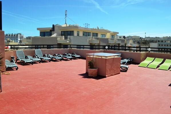 A rooftop terrace with sun loungers, a small table, and a potted plant.