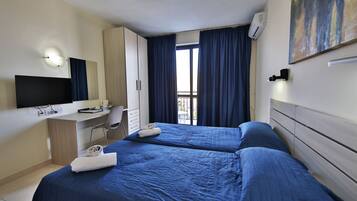 A hotel room with two beds, a desk, a chair, a TV, and a window with curtains.
