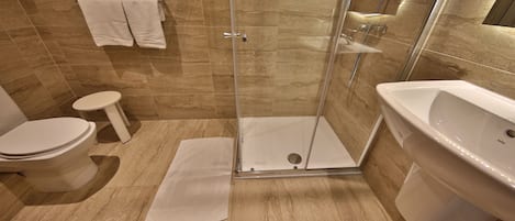 Uma casa de banho moderna com cabine de duche em vidro, uma sanita e uma pia branca.