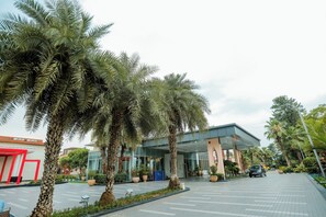 A modern building with a glass entrance, surrounded by palm trees and potted plants. - Oodles Hotel Chhattarpur South Delhi (New Delhi)