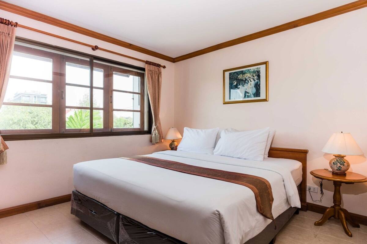 A hotel room with a large bed, two bedside tables, a window with curtains, and a framed picture on the wall.