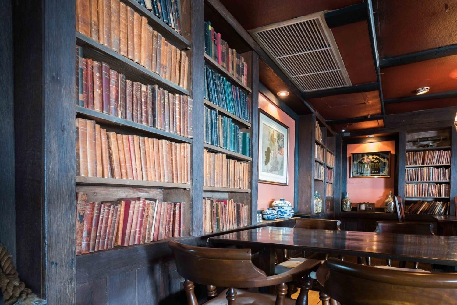 A library with bookshelves filled with books, a wooden table, and chairs.