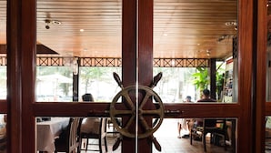 A restaurant with a wooden interior, a ship's wheel decoration, and outdoor seating visible through large windows.