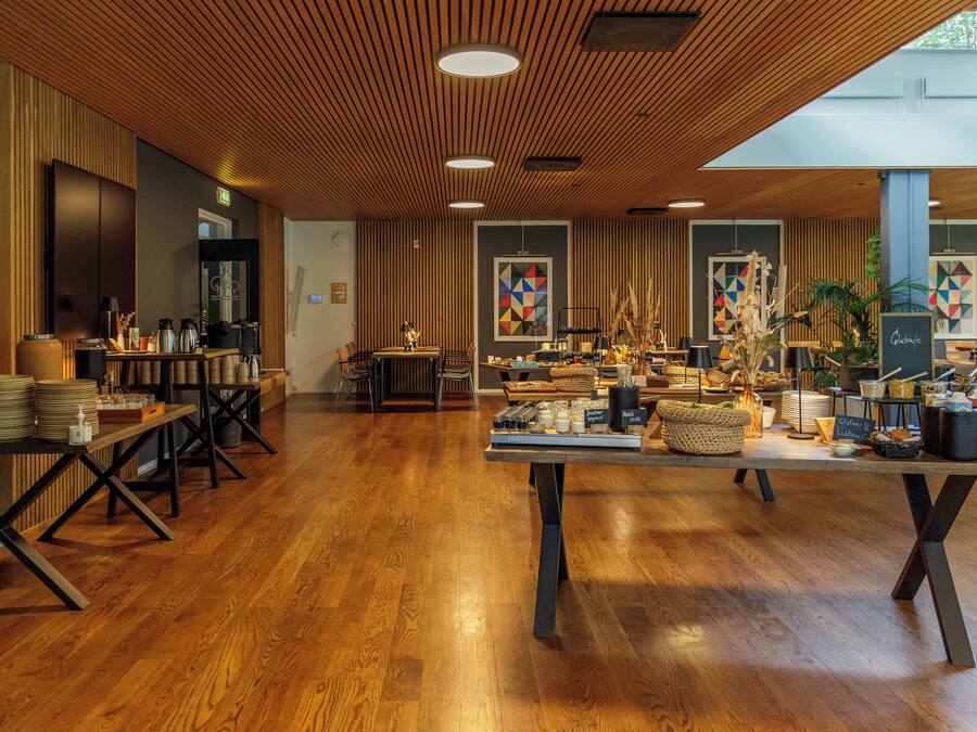 Un interior moderno con suelo de madera, una mesa central con diversos objetos y una pared con arte geométrico.