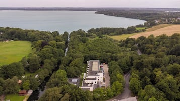 An aerial view of a property with a large building surrounded by dense greenery and a lake in the background.