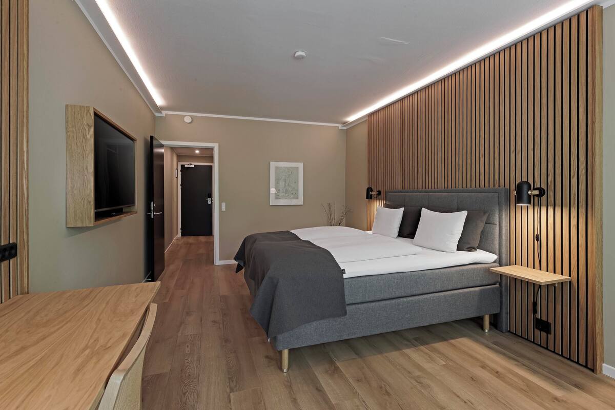 Ein modernes Schlafzimmer mit einem großen Bett, einem an der Wand befestigten Fernseher und einer Wandverkleidung aus Holz.