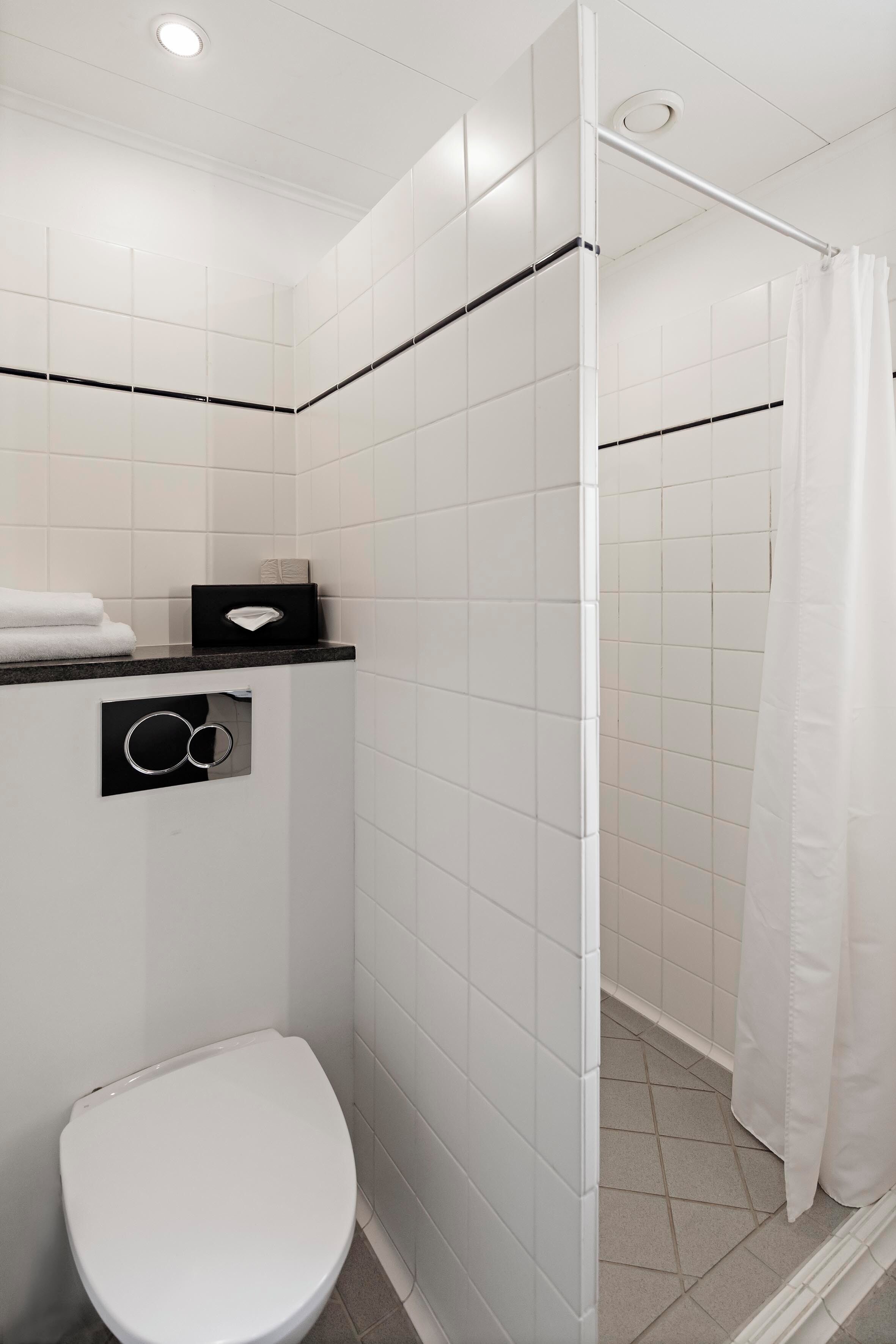 A bathroom with a white toilet, a shower with a white curtain, and a towel rack with folded towels.