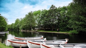 Een rij kleine bootjes afgemeerd langs een rivieroever, met een gebouw en bomen op de achtergrond.