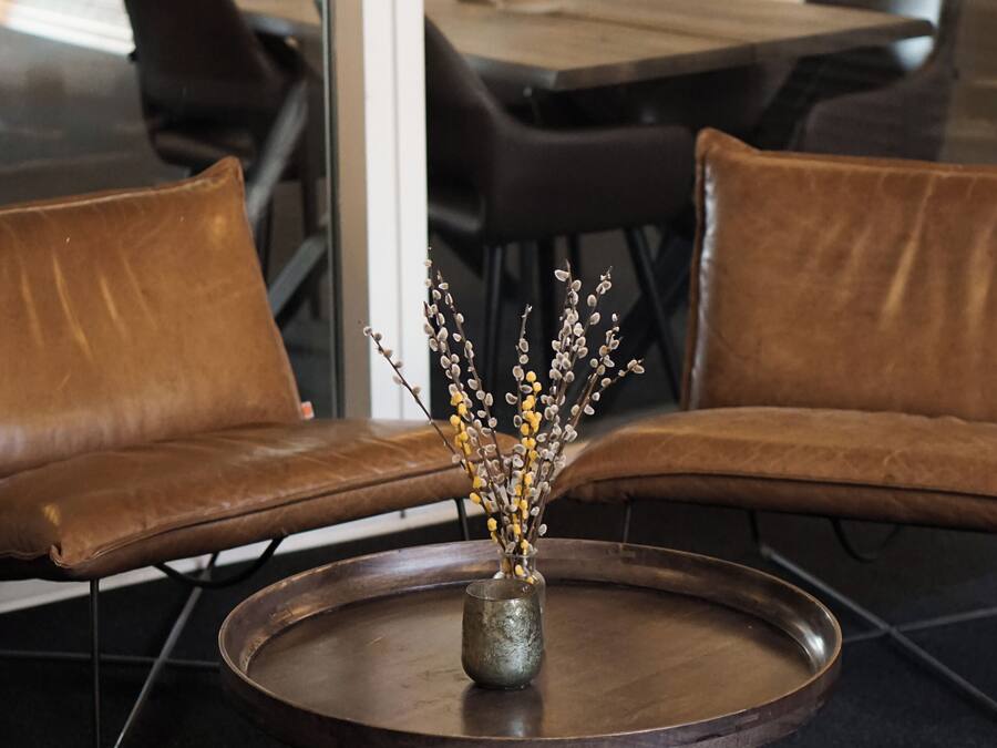 A modern interior with leather sofas, a round table with a vase of dried flowers, and a brick wall in the background.