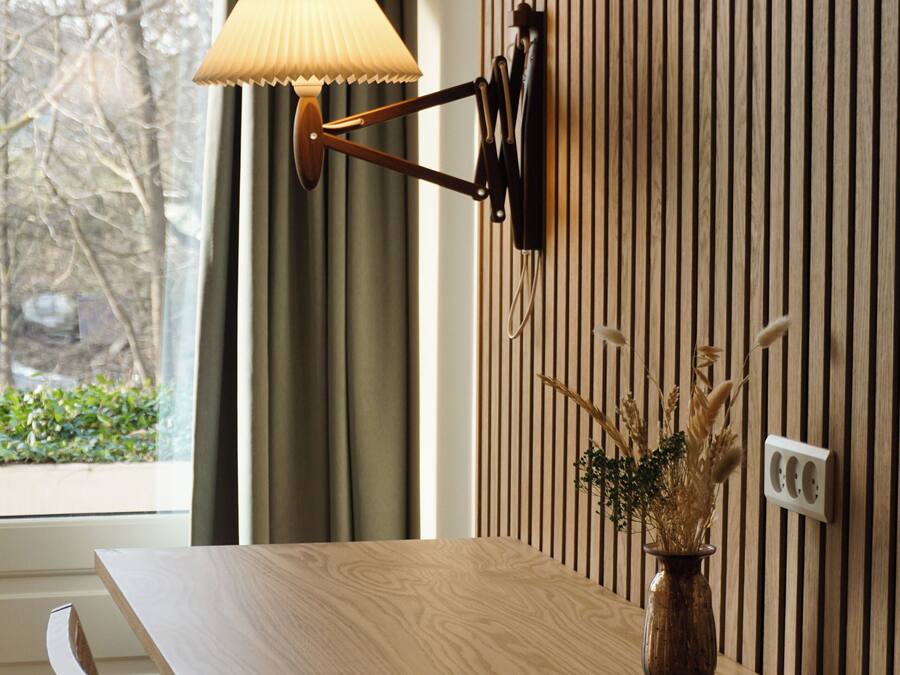Ein Holztisch mit einer Lampe, einer Vase mit Trockenpflanzen und einer Tastatur auf einem an der Wand befestigten Regal.
