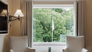 Een kamer met twee fauteuils, een tafeltje, een lamp en een raam met gordijnen.