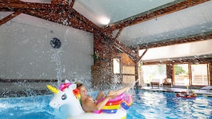 A person in a pool with a unicorn float, wooden beams, and a view of the outside.