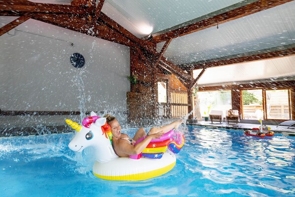 Una persona en una piscina con un flotador de unicornio, vigas de madera y vistas al exterior.