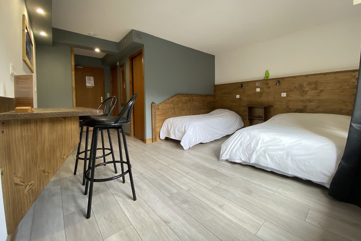 A room with two beds, a wooden headboard, a bar area with stools, and a light-colored wooden floor.