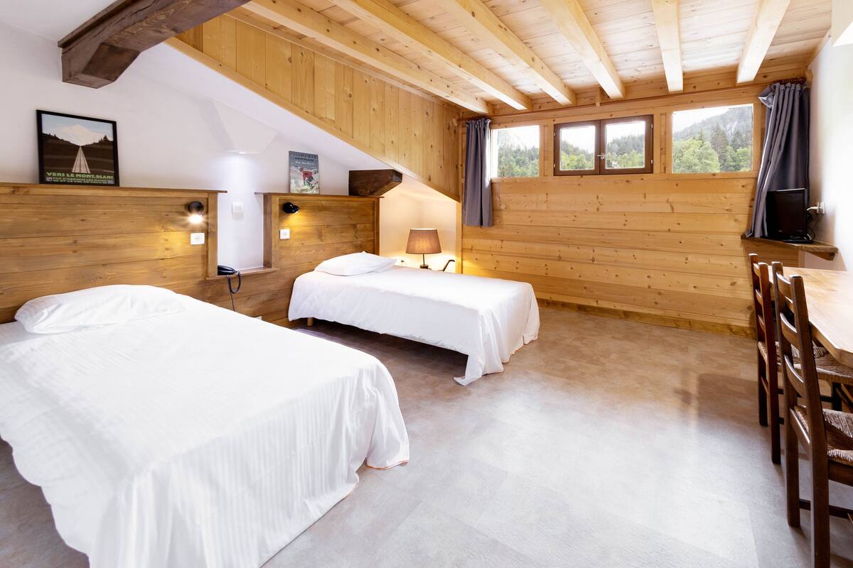 A cabin with two beds, a wooden ceiling, and a dining area with chairs.