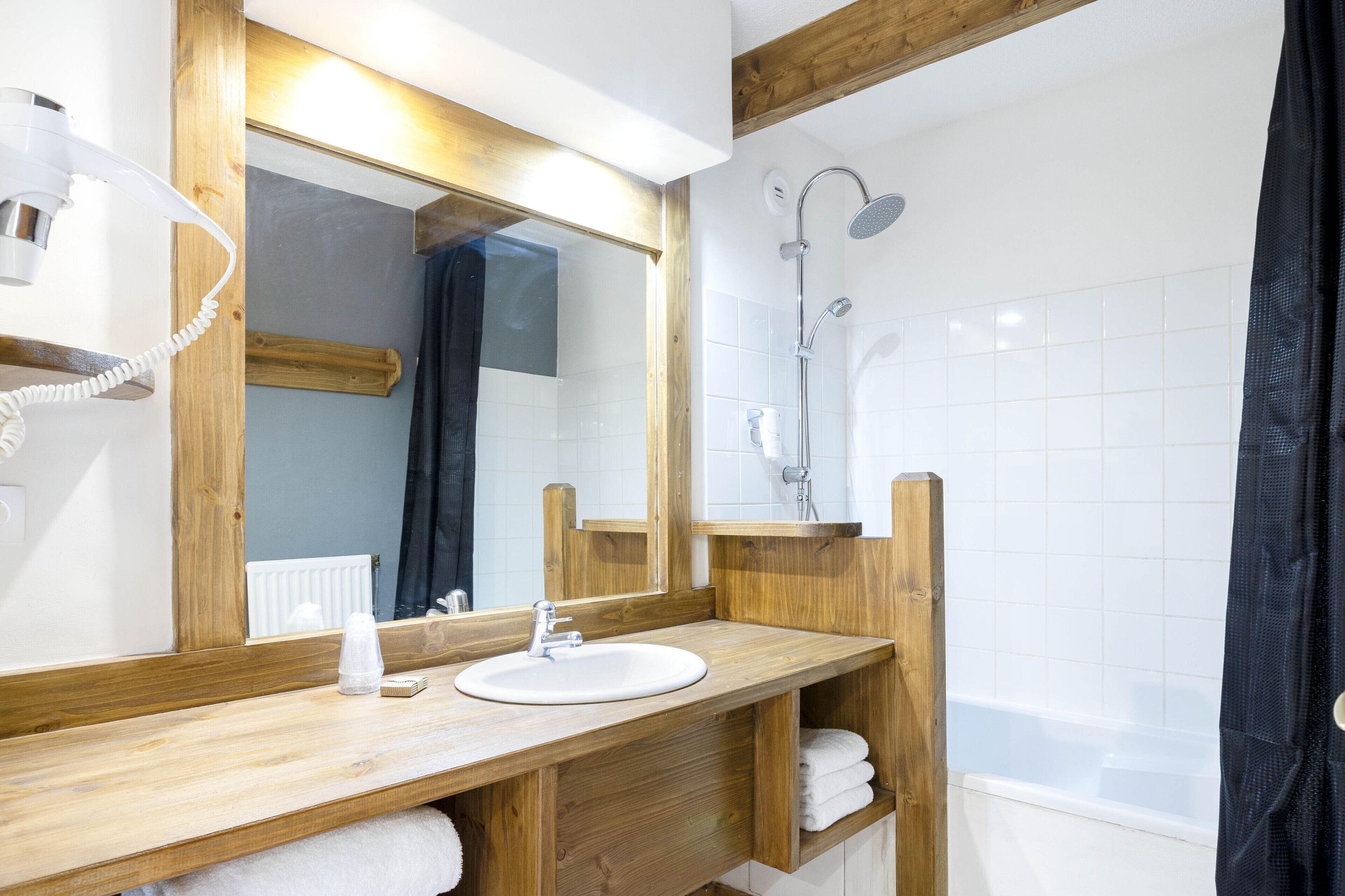 A bathroom with a wooden vanity, a large mirror, a white sink, a shower, and a towel rack.