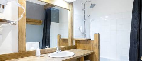 A bathroom with a wooden vanity, a large mirror, a white sink, a shower, and a towel rack.