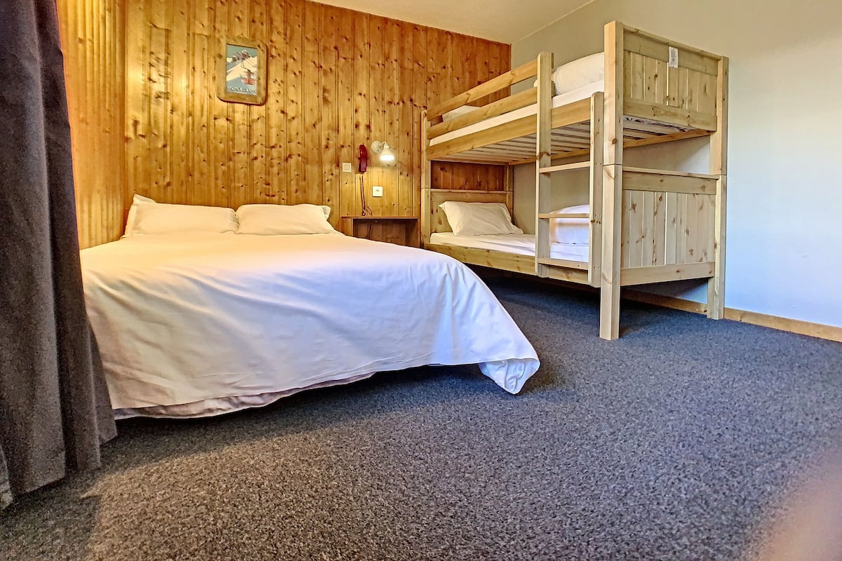 A room with a wooden bunk bed, a single bed, and a small bedside table with a lamp.