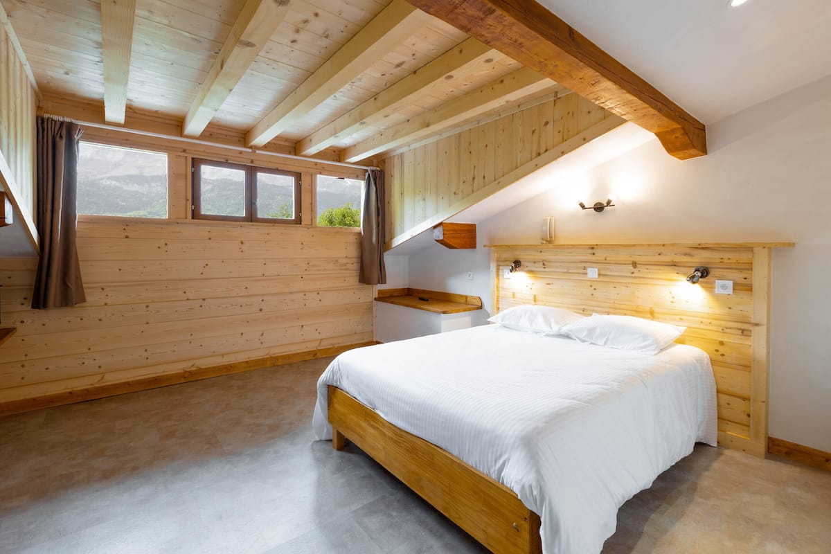 A wooden cabin bedroom with a bed, windows, and a wooden headboard.