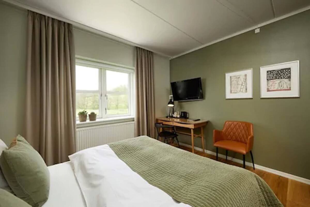 Habitación de hotel con cama, escritorio, silla, televisión y dos cuadros en la pared.