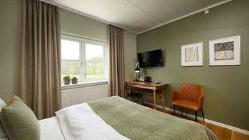 A hotel room with a bed, a desk, a chair, a television, and two framed pictures on the wall.