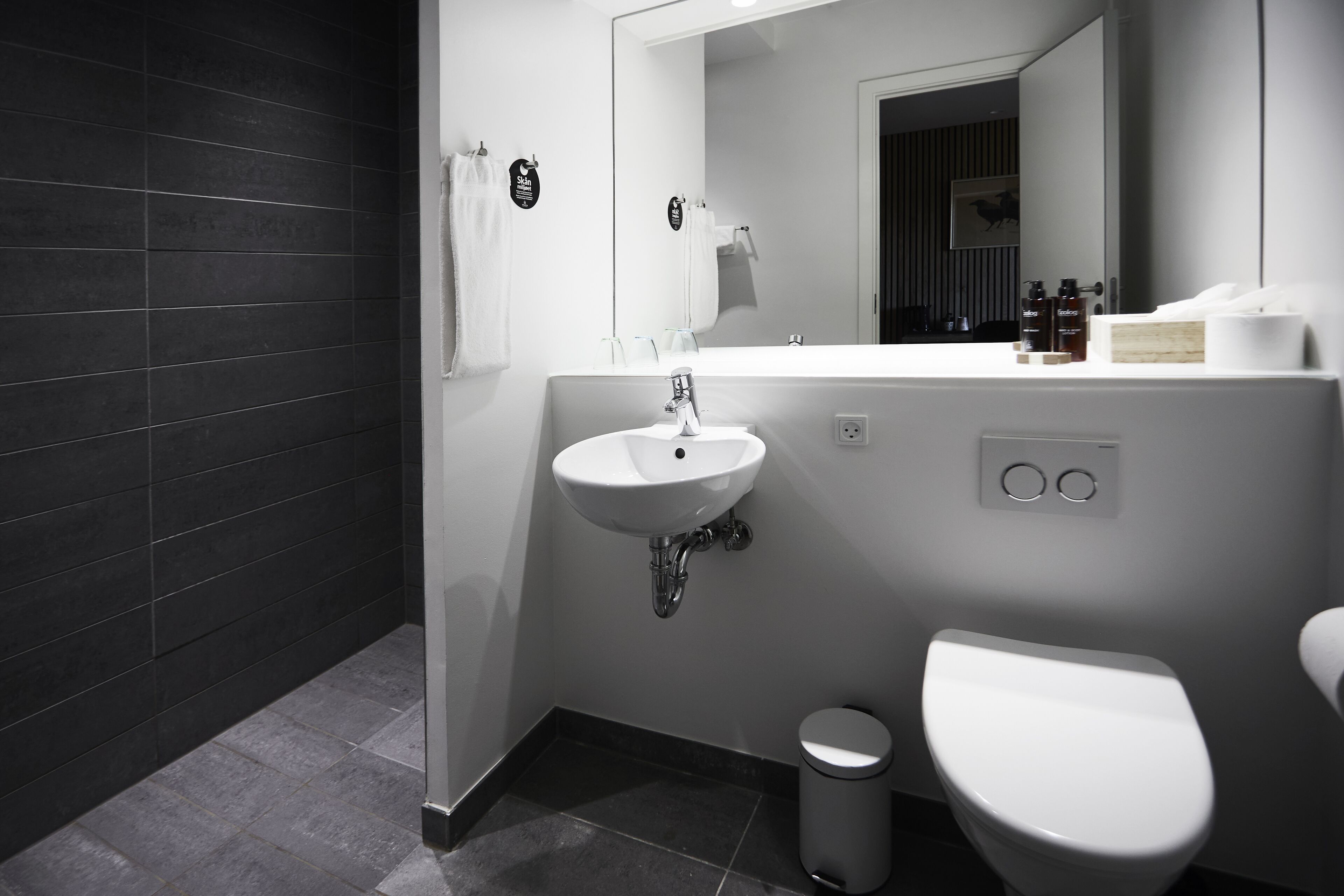 Un baño moderno con lavamanos, espejo y retrete blancos.