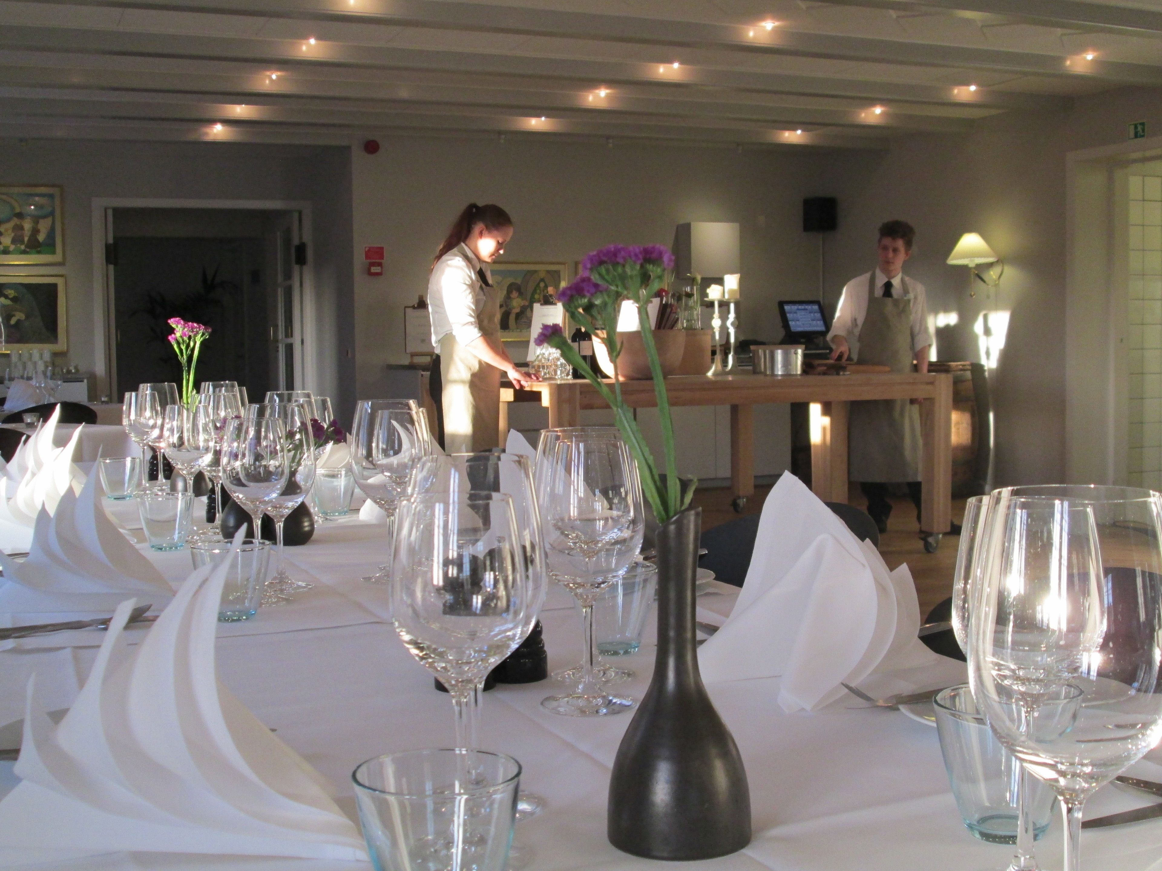 A dining area with tables set for a meal, a server attending to guests, and a bar area in the background.