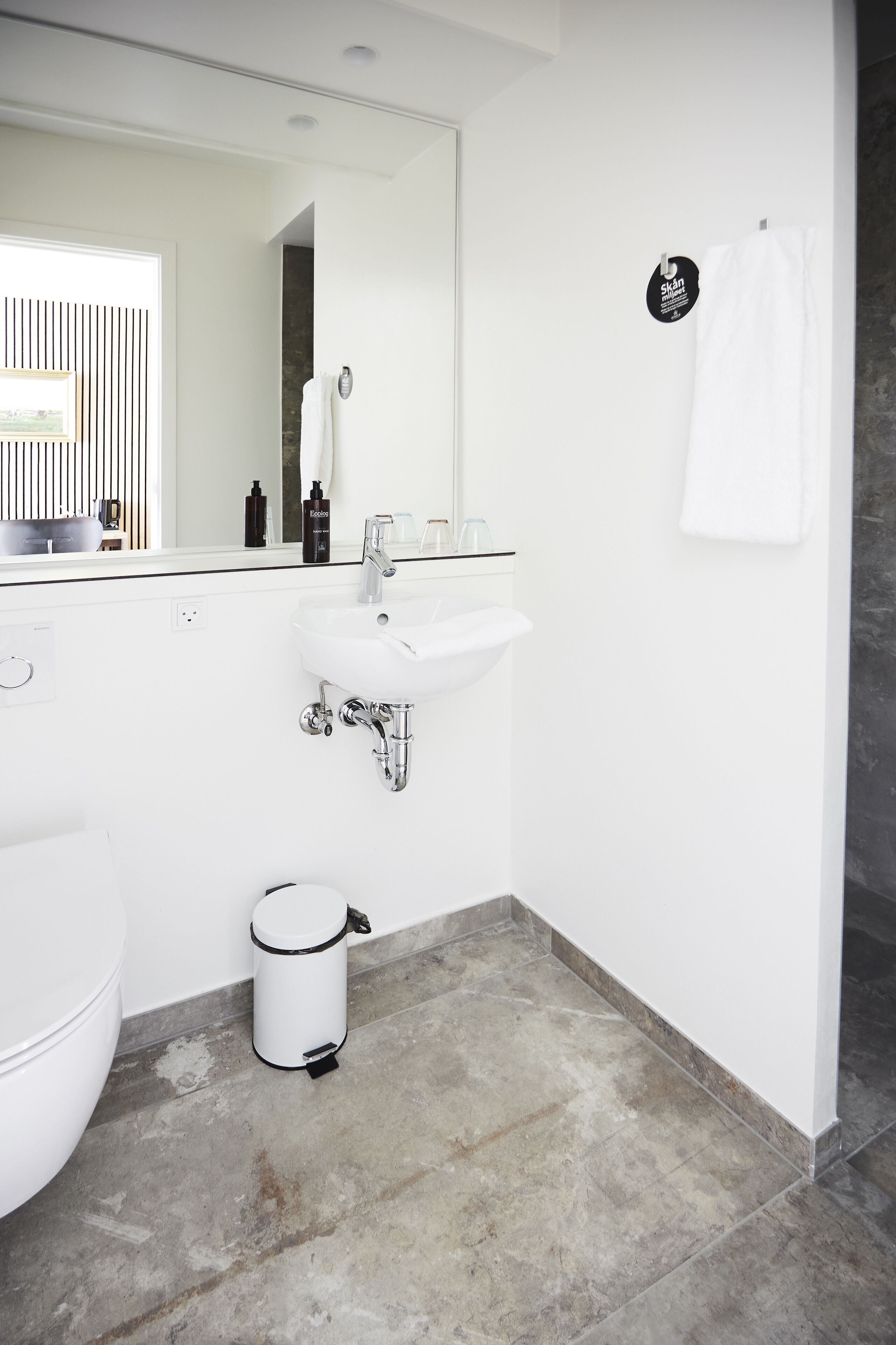 A modern bathroom with a white sink, a toilet, and a trash can.
