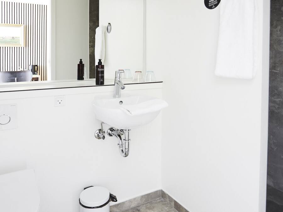 A modern bathroom with a white sink, a toilet, and a trash can.