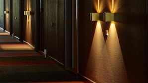 Un pasillo de hotel con piso alfombrado, pared de madera y luminarias fijadas a la pared.