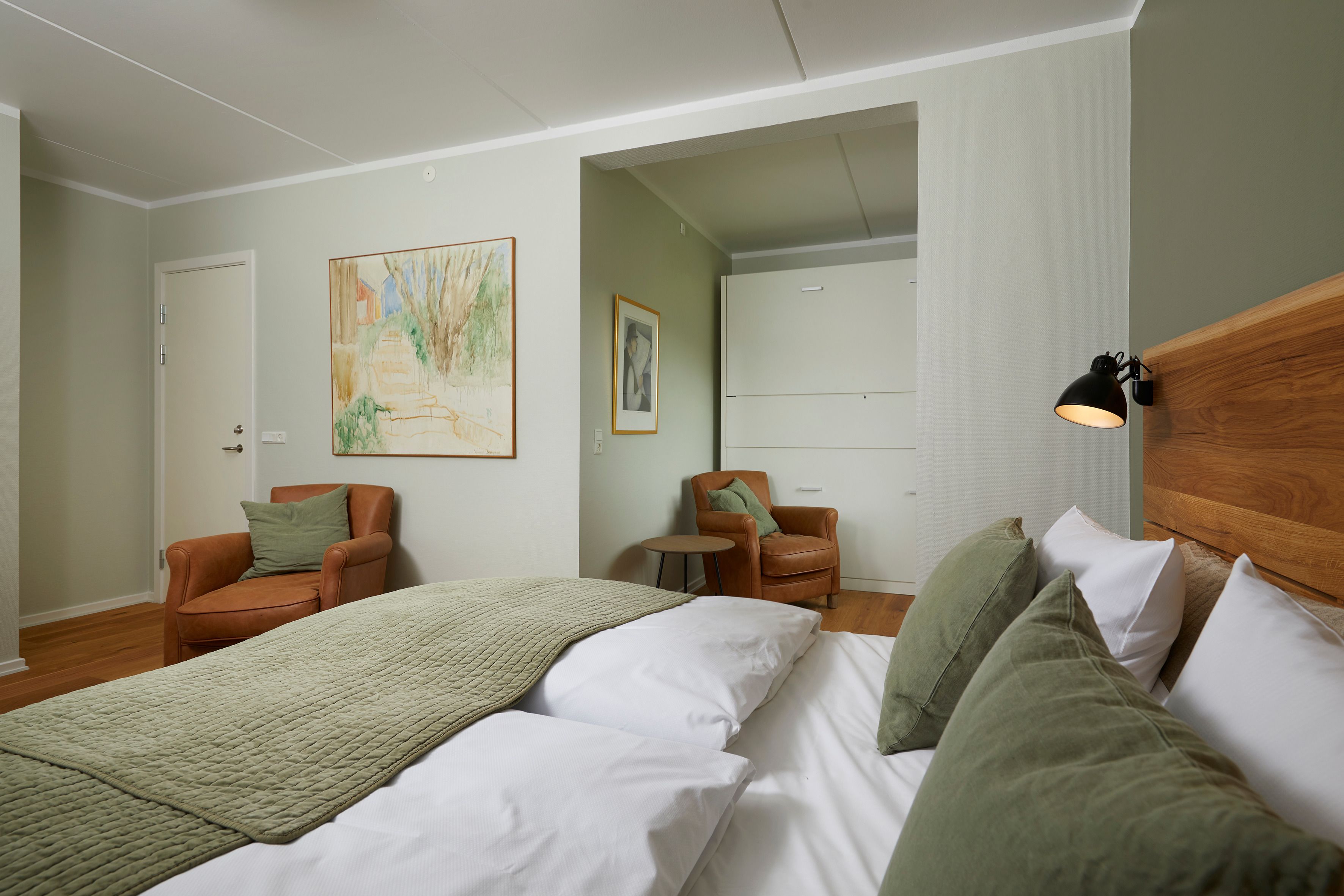A hotel room with a bed, two chairs, a small table, and artwork on the walls.