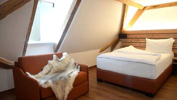 A bedroom with a wooden ceiling, a bed with white bedding, and a fur-covered chair.