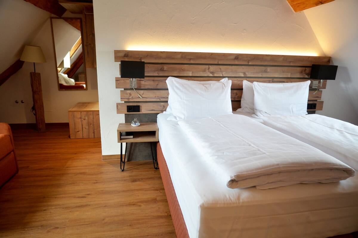 A bedroom with a wooden headboard, a bed with white bedding, a nightstand with a lamp, and a red chair.
