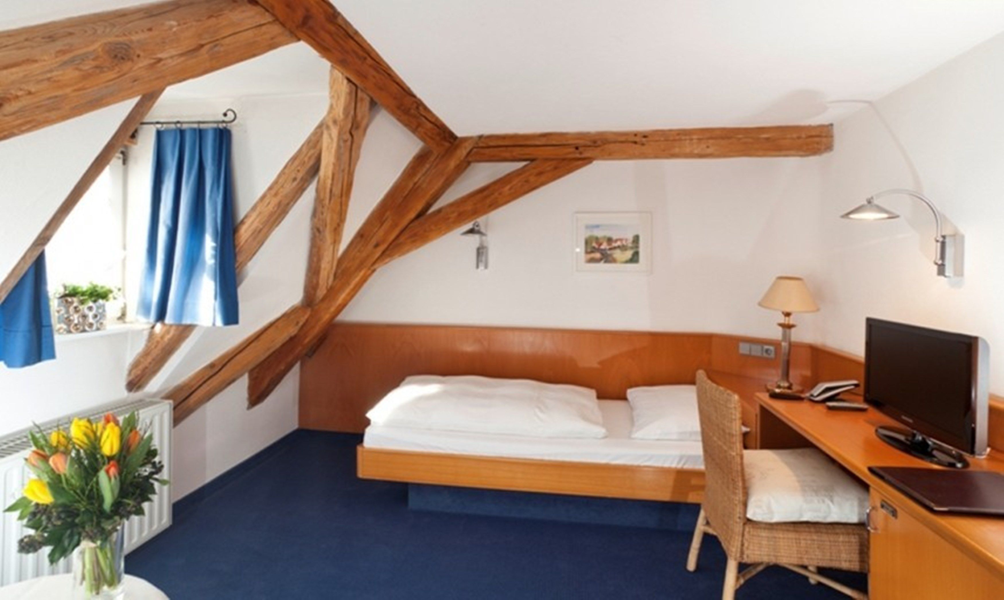 Una camera da letto con soffitto in legno, un letto, una scrivania con un computer, una sedia e una finestra con tende.
