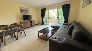 A living room with a sofa, a coffee table, a TV on a wooden cabinet, and a dining area with chairs and a table. - Jomtien Beach Residence (Pattaya)