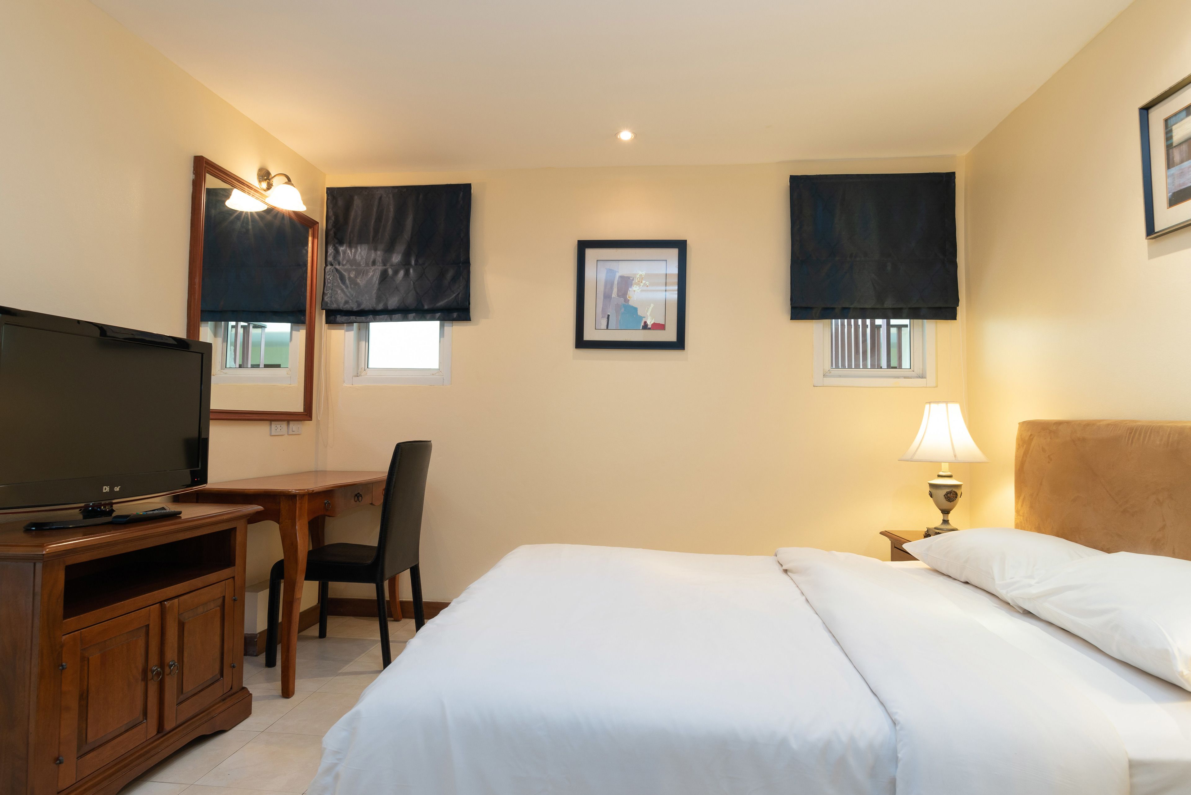 A hotel room with a bed, a desk with a chair, a television, and a framed picture on the wall.