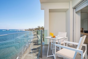 A balcony with a clear view of the ocean, a table with chairs, and a breakfast setup.