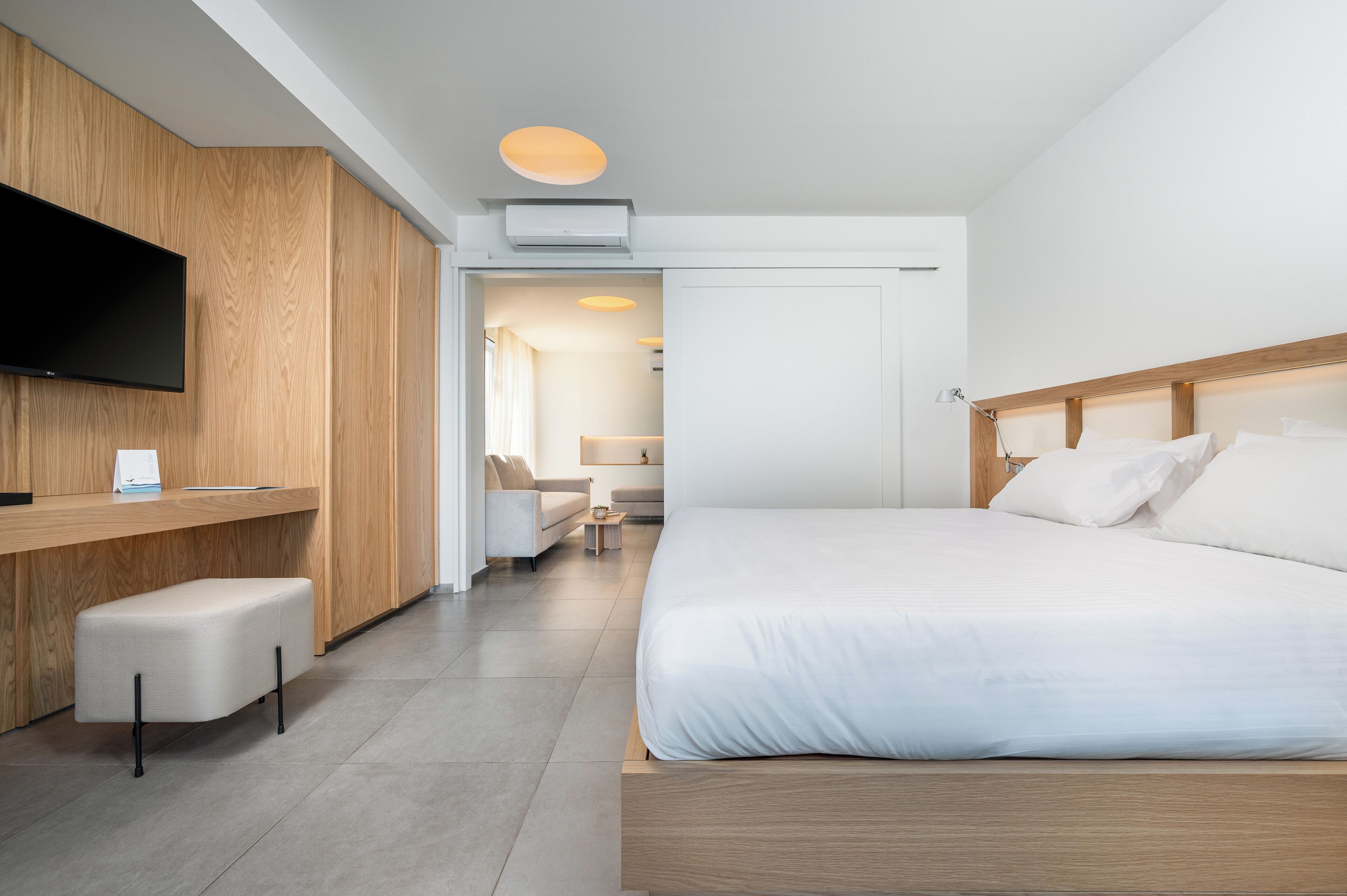 Een moderne hotelkamer met een houten bureau, een flatscreen televisie, een bed met witte lakens en een zithoek.
