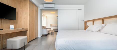 Een moderne hotelkamer met een houten bureau, een flatscreen televisie, een bed met witte lakens en een zithoek.