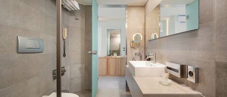A modern bathroom with a toilet, sink, and shower area, featuring a glass door and a large mirror.